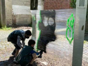 2 Jungs sprayen ein Motiv an eine Folien-Leinwand