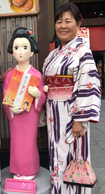 Naoko Riekötter im Kimono steht lächelnd neben einer kleineren Figur ebenfalls im Kimono
